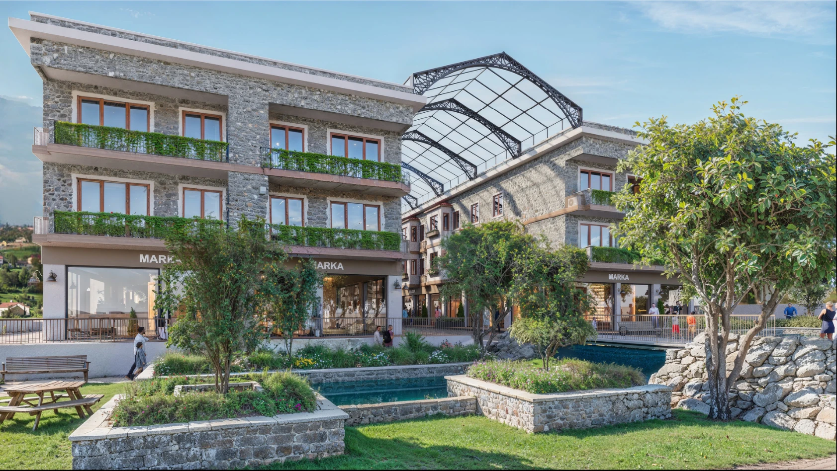 Resim, doğal bir ortamda yer alan modern bir otel veya konaklama tesisini göstermektedir. Bina, taş yüzeyler ve geniş pencerelerle tasarlanmış olup, yeşil bitki örtüsüyle çevrilidir. Ön planda, düzenli bahçeler ve su elementleriyle donatılmış bir açık alan yer almaktadır. Arkada ise, yapının mimarisine zarif bir dokunuş katan, camdan bir çatı dikkat çekmektedir. Genel atmosfer, huzurlu ve şık bir tatil ortamı sunmaktadır.
