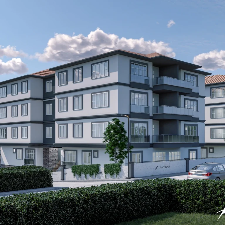 Bu görsel, modern mimari tarzda tasarlanmış bir apartman blokunu göstermektedir. Geniş pencereleri ve şık cephesiyle dikkat çeken yapı, yeşil bir peyzaj içerisinde yer almakta. Etrafta yer alan ağaçlar ve çalılar, doğal bir çevre sunarak sakin bir yaşam alanı yaratmaktadır. Apartmanın cephesinde yer alan 'AS TROVA' logosu, projeye ait kimliği vurgulamaktadır. Güneşli bir günde çekilmiş olan bu resim, sakin ve konforlu bir yaşam alanının estetiğini yansıtmaktadır.