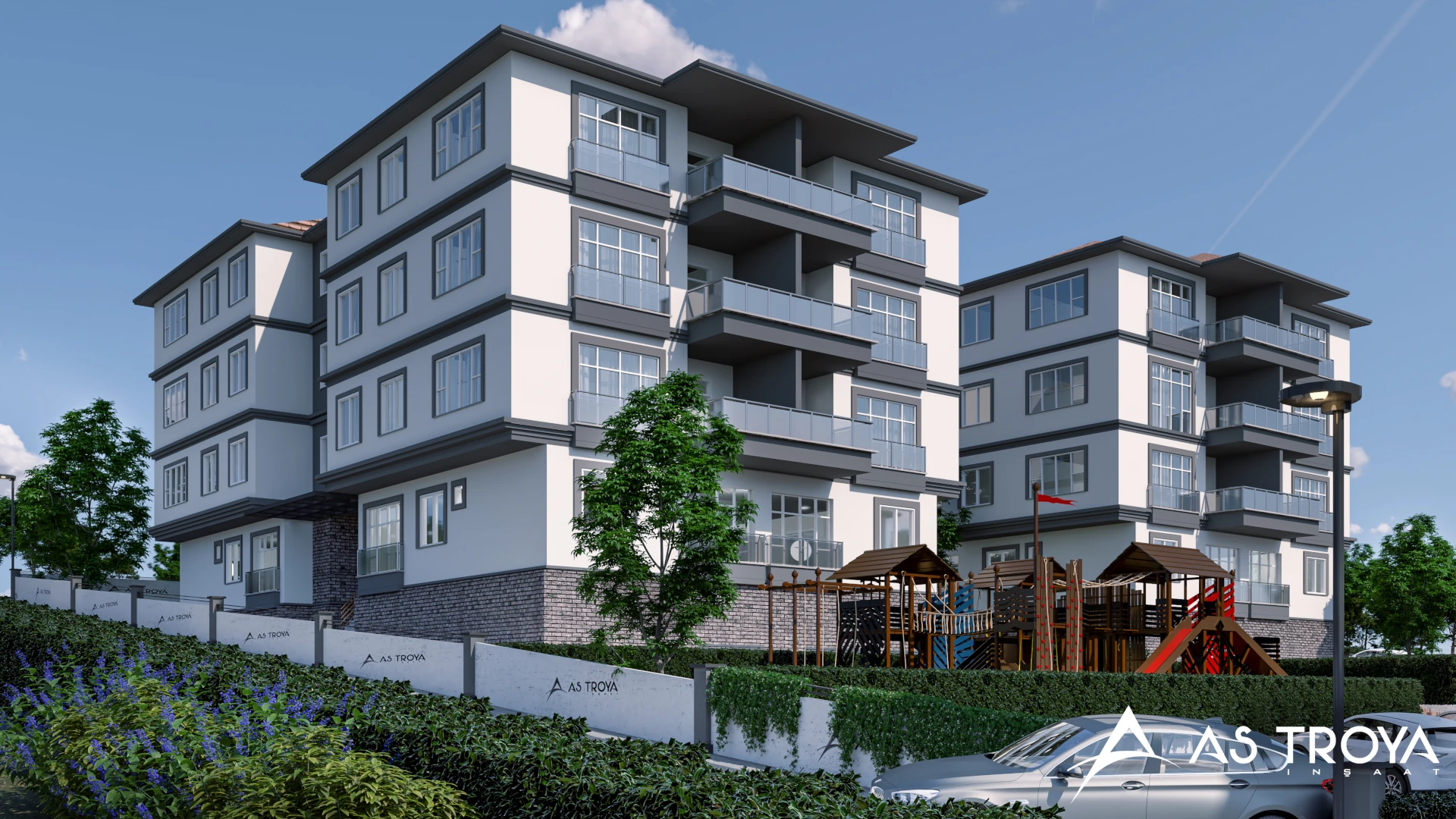 Modern mimariye sahip çok katlı konut bloklarının dış cephe görünümü. Geniş cam balkonlar, gri-beyaz tonlarda cephe kaplaması ve düzenli peyzaj alanları dikkat çekiyor. Ön bölümde çocuk oyun parkı ve otopark alanı yer alıyor. Çevresi yeşilliklerle çevrili site giriş duvarında ‘As Troya İnşaat’ logosu bulunuyor.