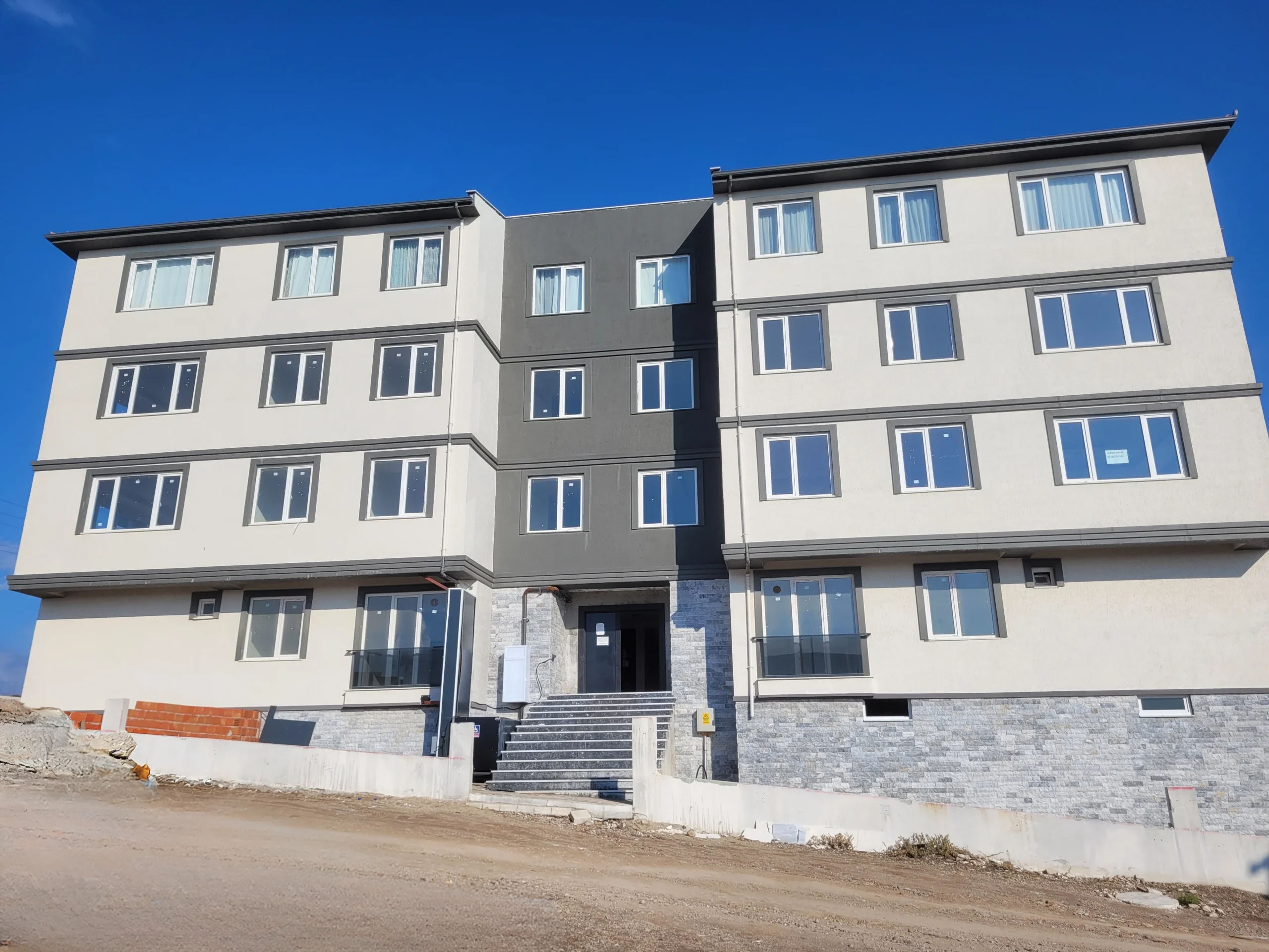 Troya Sitesi projesine ait 4 katlı modern konut bloğunun dış cephesi, tamamlanma aşamasında. Geniş pencereler, modern cephe kaplaması ve merkezi giriş bölümü görülmektedir.