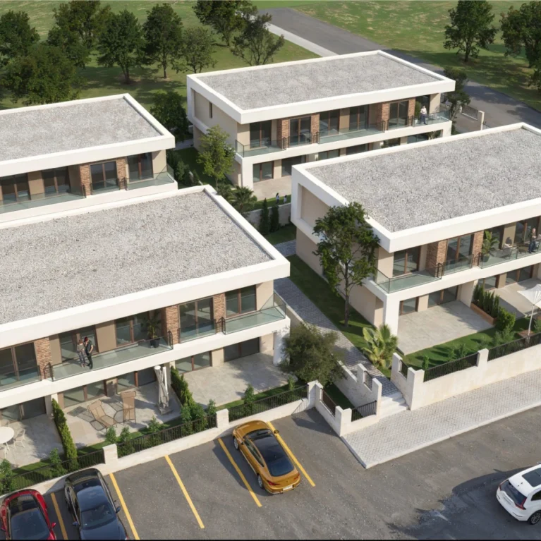 Bu görüntüde, modern mimari tarzında tasarlanmış üç adet villa yer alıyor. Villalar, geniş terasları ve yeşil alanları ile dikkat çekiyor. Çevresinde ağaçlar ve peyzaj düzenlemesi bulunan bu konutlar, sakin bir yaşam alanı sunuyor. Ayrıca, park alanı ile birlikte düzenlenmiş bir yol da görülüyor, bu da araçların rahatça park edilebileceğini gösteriyor.